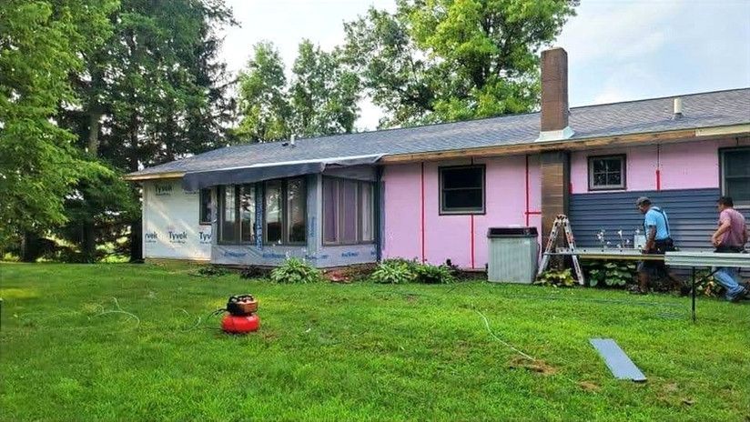 House exterior under construction, pink insulation, blue siding, men working, grass yard.