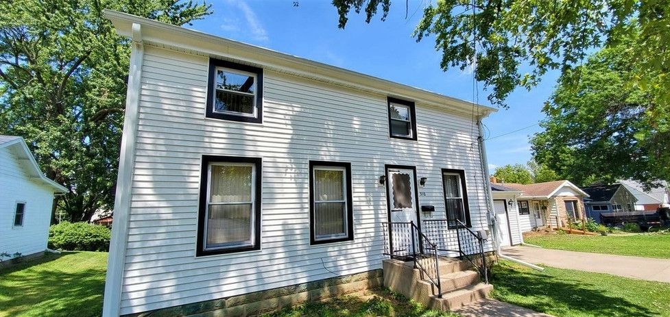 White two-story house with black-trimmed windows. Front porch and yard with trees.