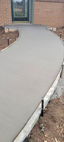 A newly poured, curved concrete walkway leading to a brick home's door.
