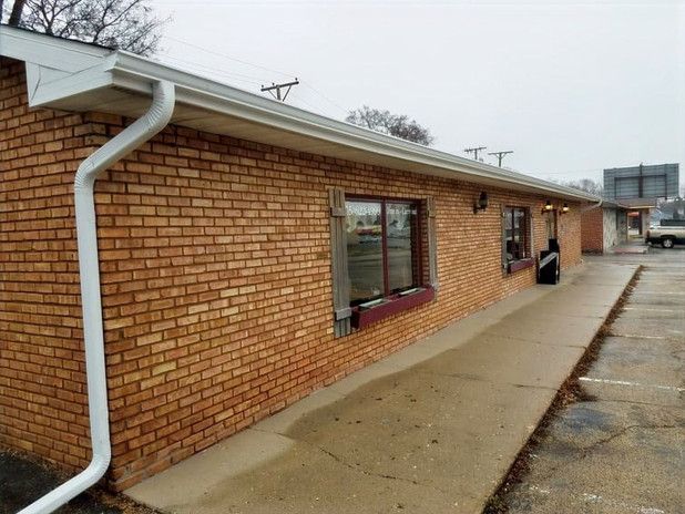 Brick building with white gutters and a sidewalk.