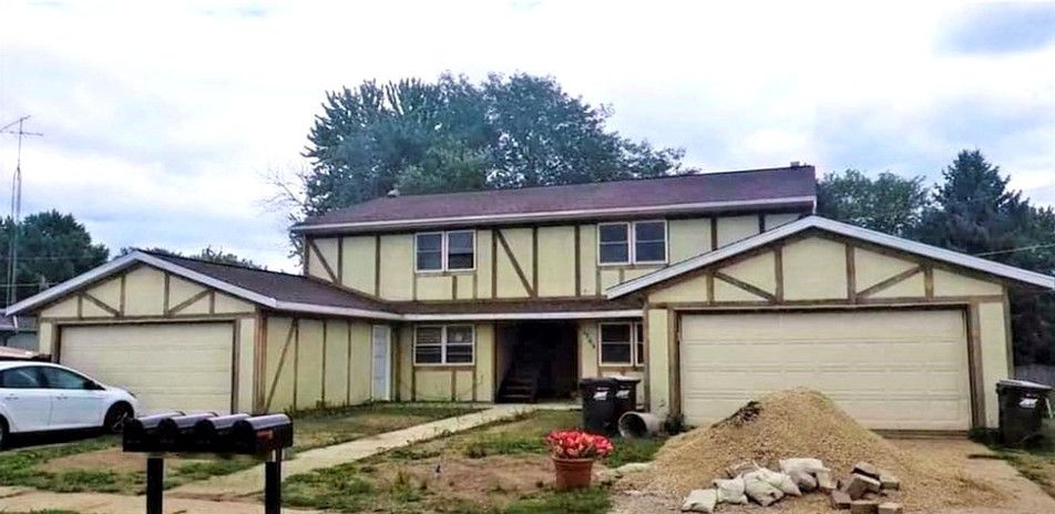 Two-story house with two garages, a front yard, and overcast sky.