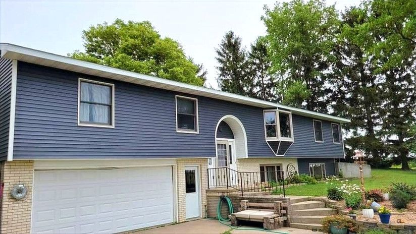 Two-story house with blue siding, a white garage door, and a brick lower level. Green lawn and trees.