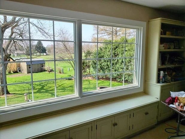 Large white-framed windows overlooking a green yard, trees, and a shed. Built-in cabinets sit below the windows.