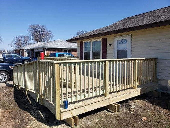 Wooden deck attached to a house with railings and a blue sky overhead.