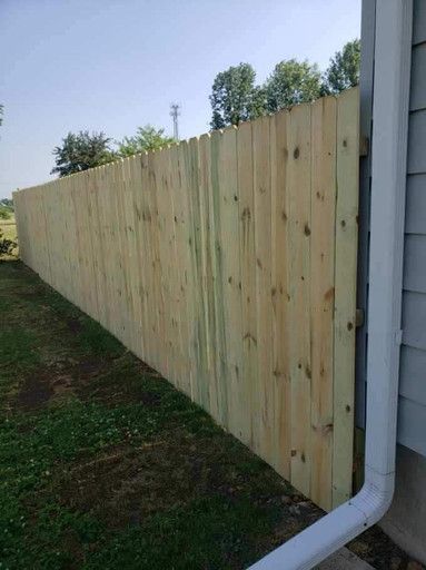 Wooden privacy fence along a house, with grass in the foreground and a white downspout visible.