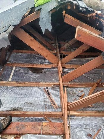 Damaged wooden roof framing exposed beneath torn gray insulation and debris
