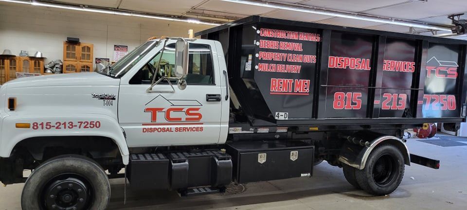 White dump truck with black bed. TCS logo on door, phone number. Black text on bed lists services.