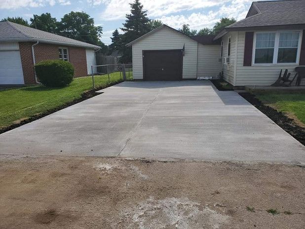 Newly poured concrete driveway in front of a house and garage on a sunny day.
