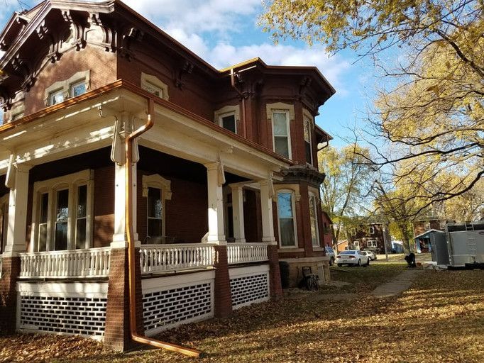Brick Victorian house with a porch and autumn foliage in a yard.