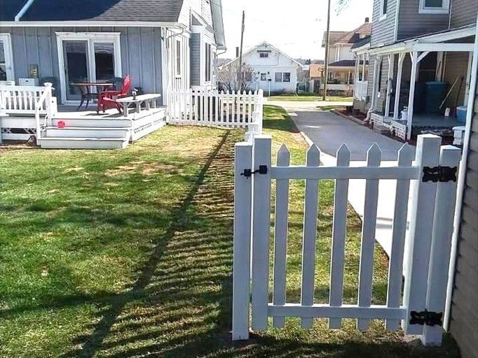 White picket fence with gate in front yard, with houses and pathway in the background.