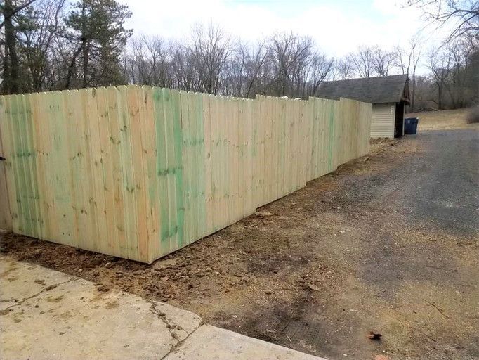 A wooden fence alongside a driveway, the wood shows some green discoloration.