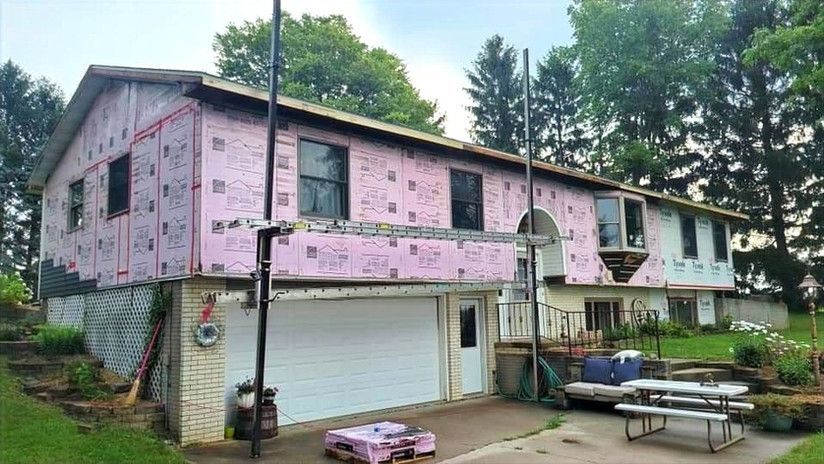 House under renovation, pink insulation exposed, garage, and yard with picnic table.