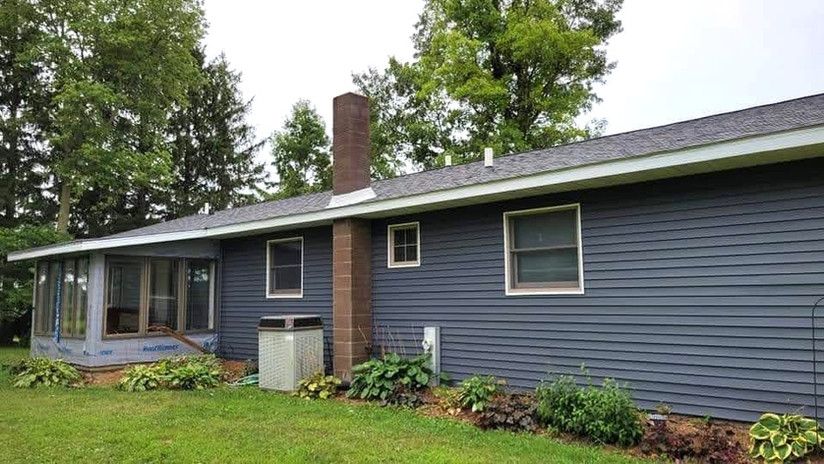 Blue-sided house with a brick chimney, screen porch, and green lawn.