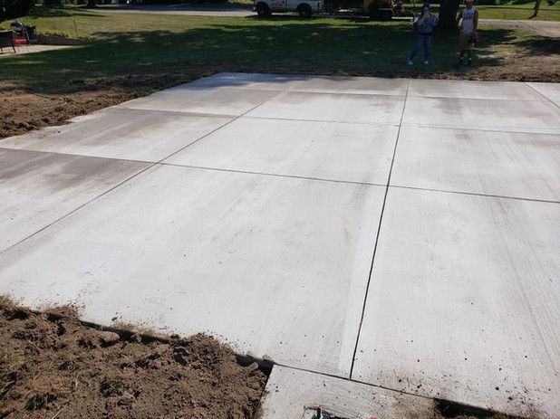 Newly poured concrete driveway with division lines, dirt edges, and two people in the background.