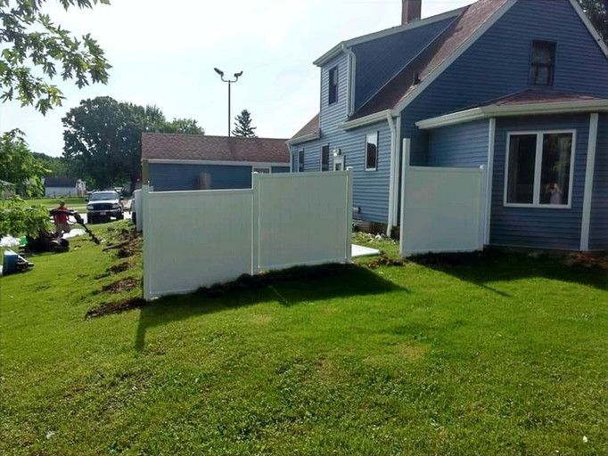 White fence partially installed beside a blue house on a green lawn.