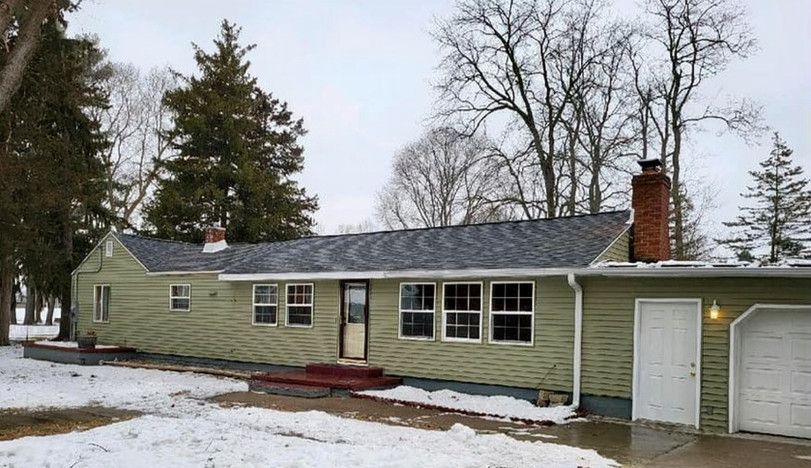 Green ranch-style house with dark roof and white trim in a snowy setting. Garage on the right.