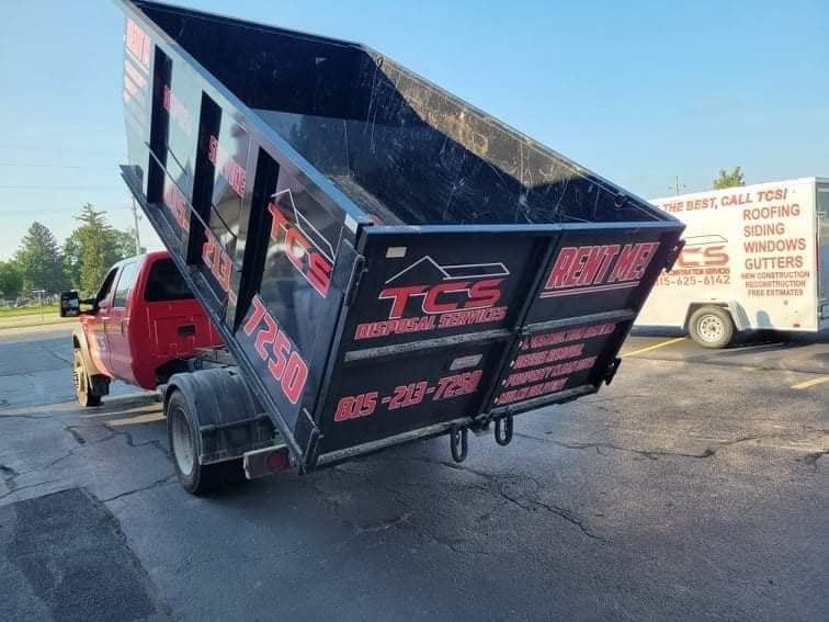 Red dump truck with raised black bed, parked on cracked pavement. A white trailer is behind it.