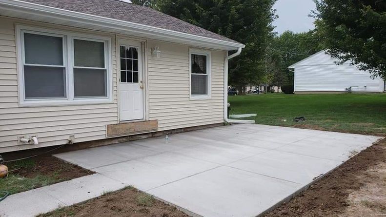 Newly poured concrete patio next to a light-colored house with a door and windows.