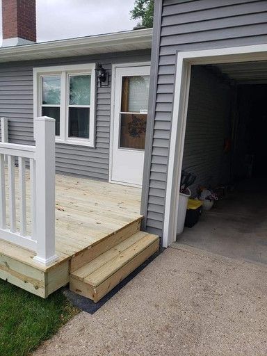 A small wooden deck with white railing and steps leading to a white door. The house has gray siding and a garage.