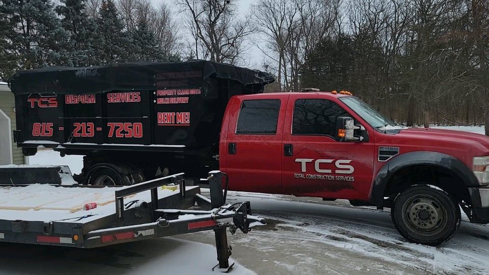 Red TCS truck with a black dump trailer, on a snowy residential street.