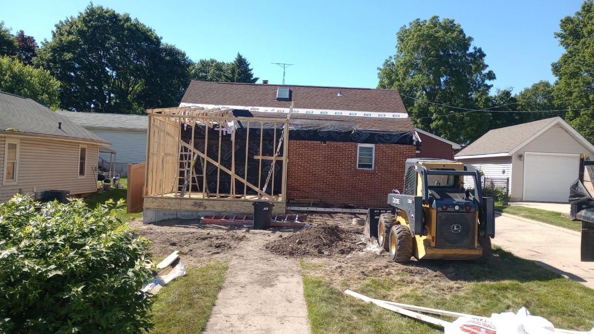 House under construction with exposed framing, a small bulldozer, and a clear sky.