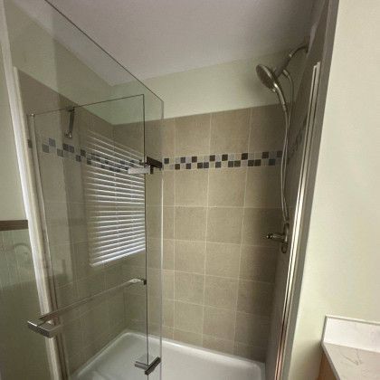 Shower stall with glass door, beige tiled walls, and silver shower head.