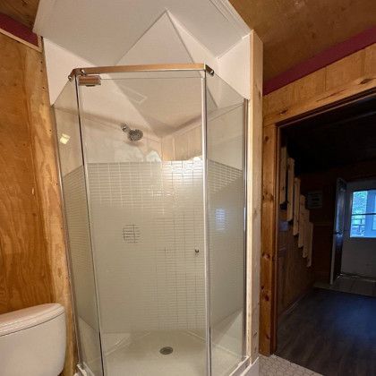 Corner shower with glass doors in a bathroom. Toilet on the left, door on the right.