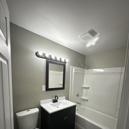 Bathroom with a black vanity, white tub, mirror, and light fixture.