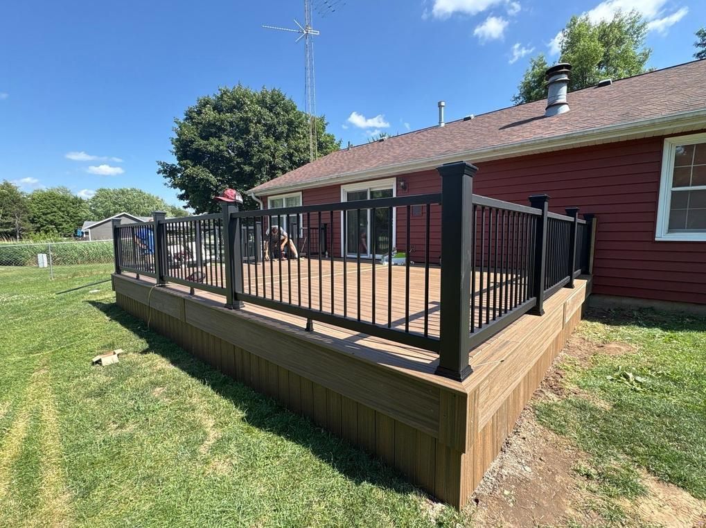 Wooden deck with black railing next to a red house on a sunny day.