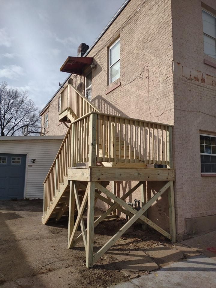 Wooden exterior staircase on the side of a brick building. The stairs lead to a deck.