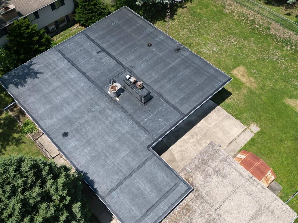 Overhead view of a flat, black roof with vents, concrete patio, and patches of green grass.