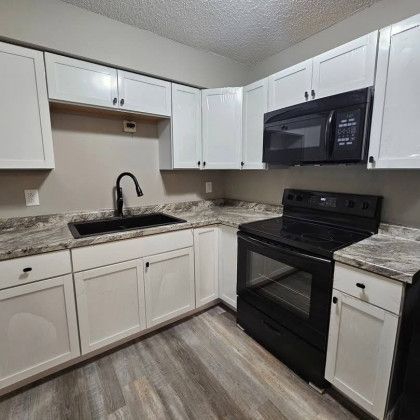 White kitchen cabinets, black appliances, granite countertops, and hardwood floors.