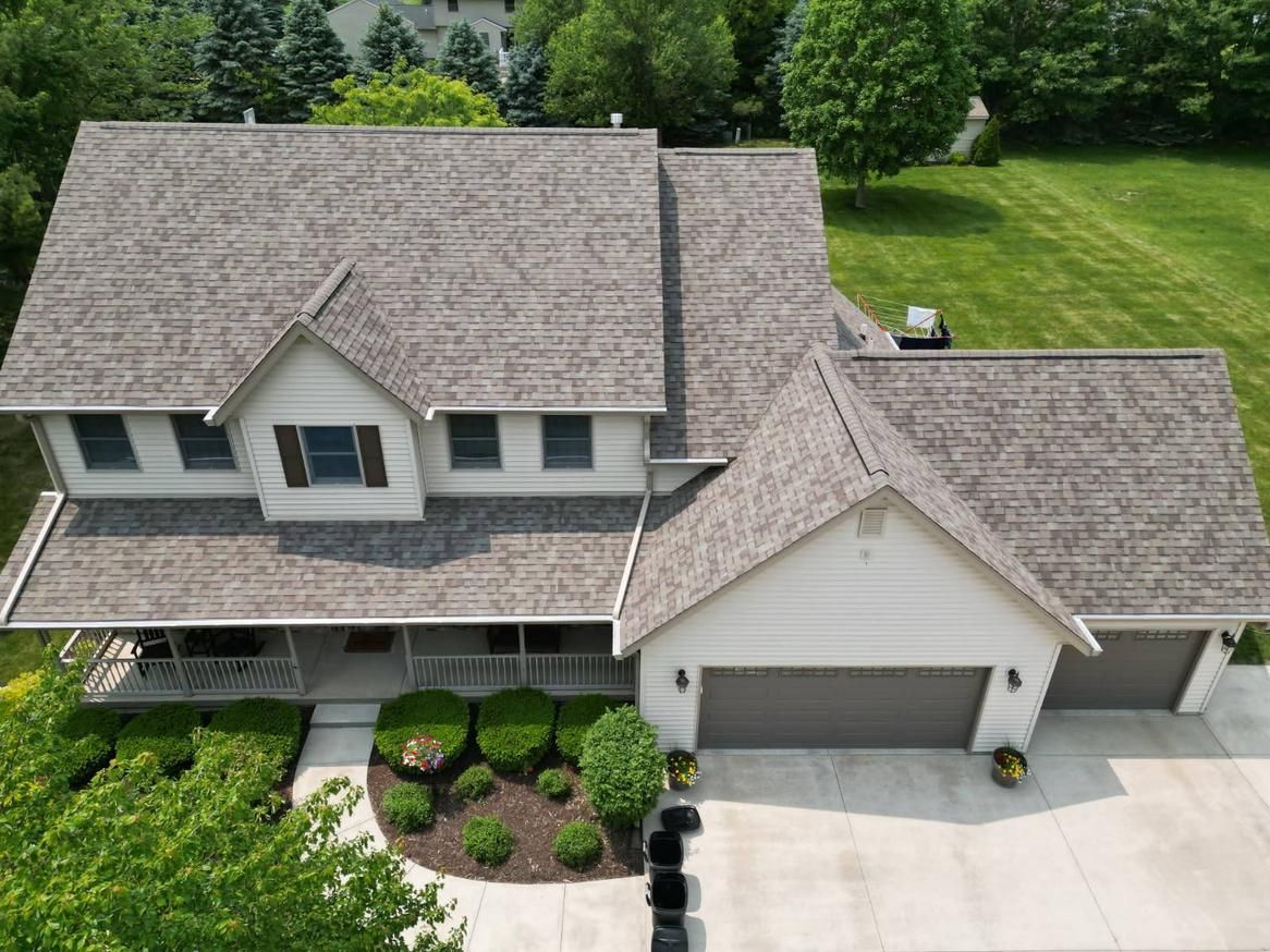Aerial view of a house with gray roof, white siding, and a two-car garage, on a green lawn.