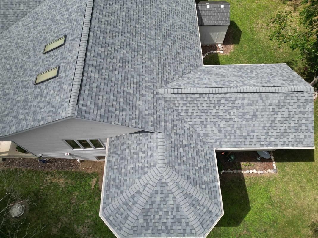 Overhead view of a house with a gray asphalt shingle roof. The house is surrounded by green grass.