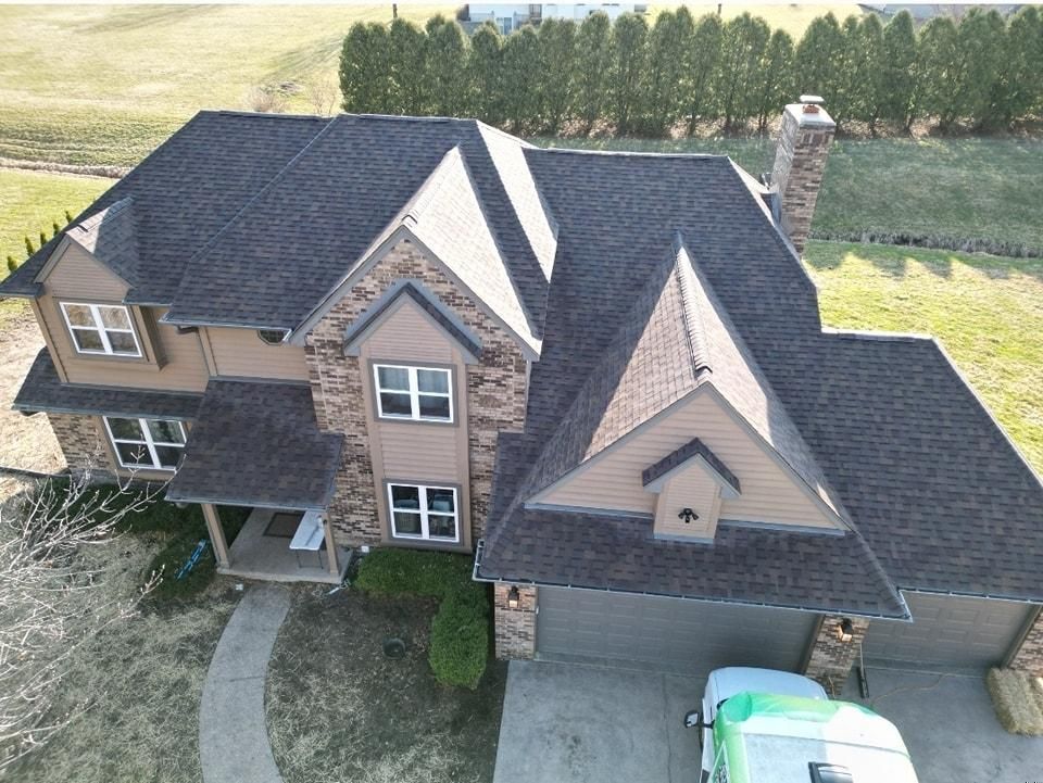 Brown shingled roof on a two-story house with stone and tan siding, a chimney, and a garage.