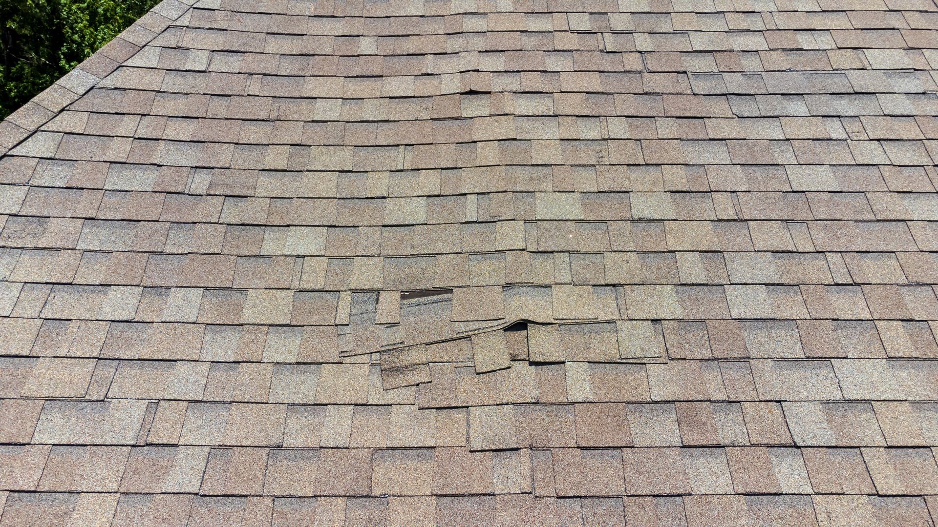 Weathered gray-brown shingle roof with patchy discoloration and a small damaged area near the center
