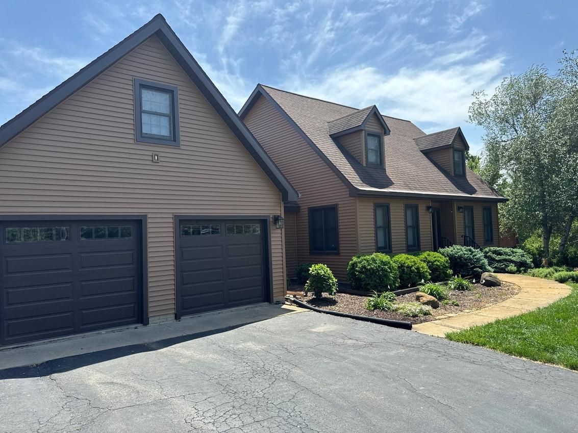 Brown house with two-car garage, driveway, and landscaping on a sunny day.