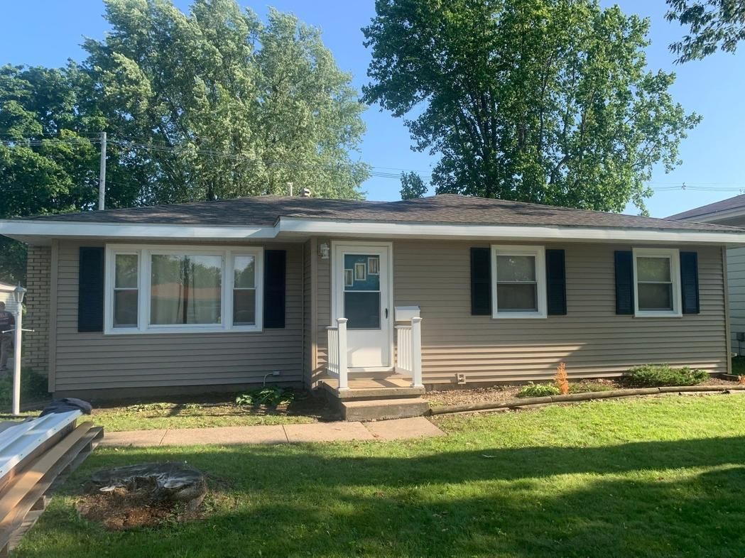 Beige ranch-style house with black shutters, a white front door, and a green lawn under a sunny sky.