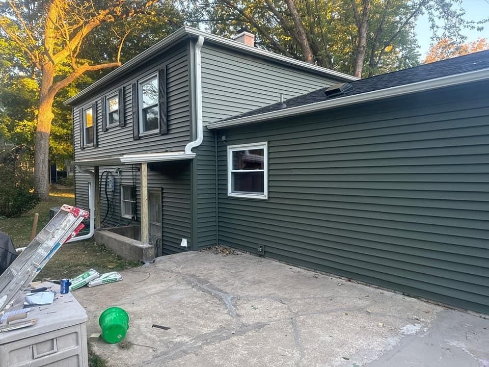 Two-story house with green siding, black shutters, and concrete patio.