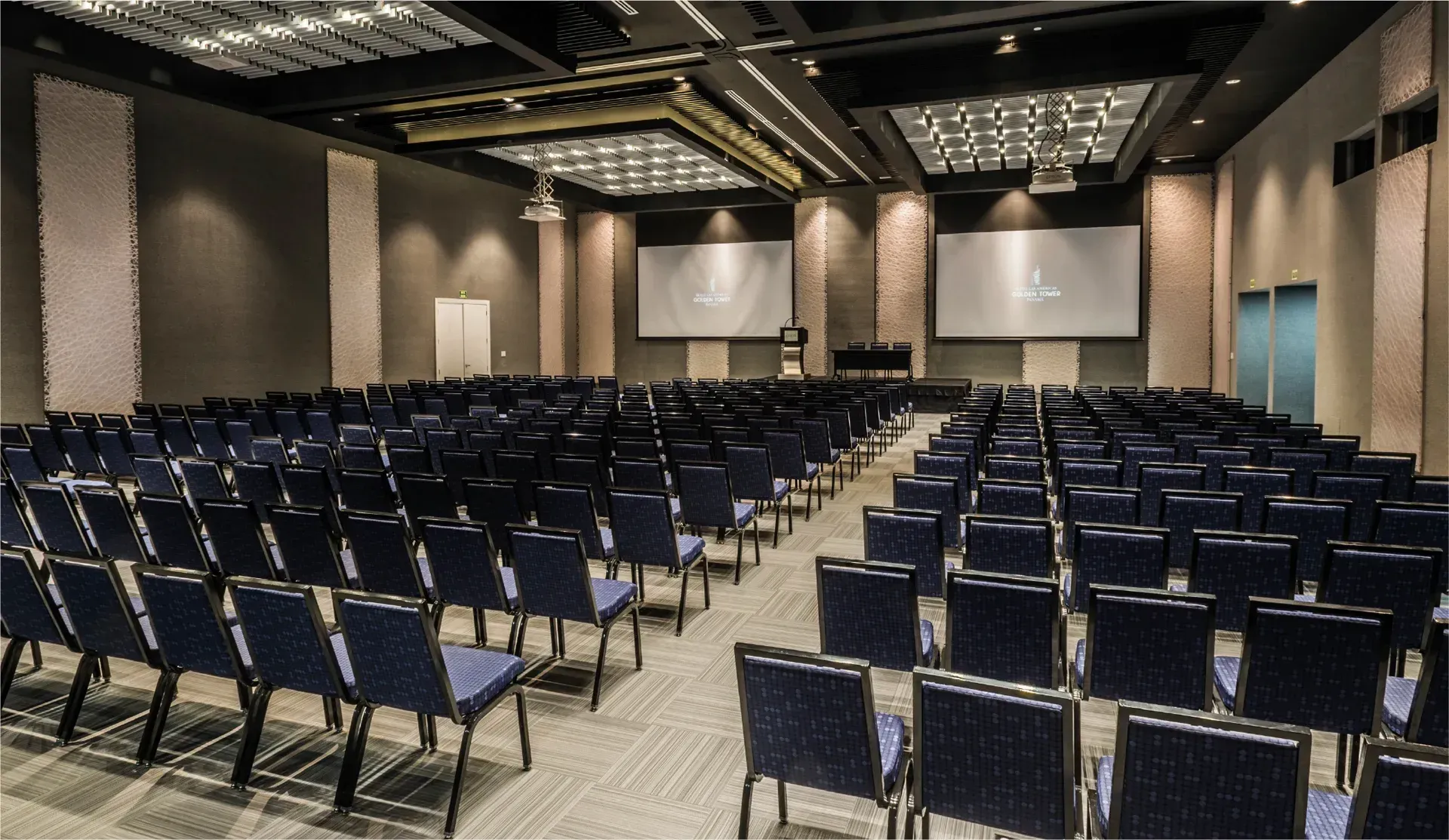 Una gran sala con hileras de sillas y una pantalla de proyección.