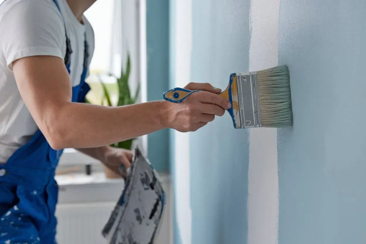 Person painting a light blue wall with a paintbrush in a room