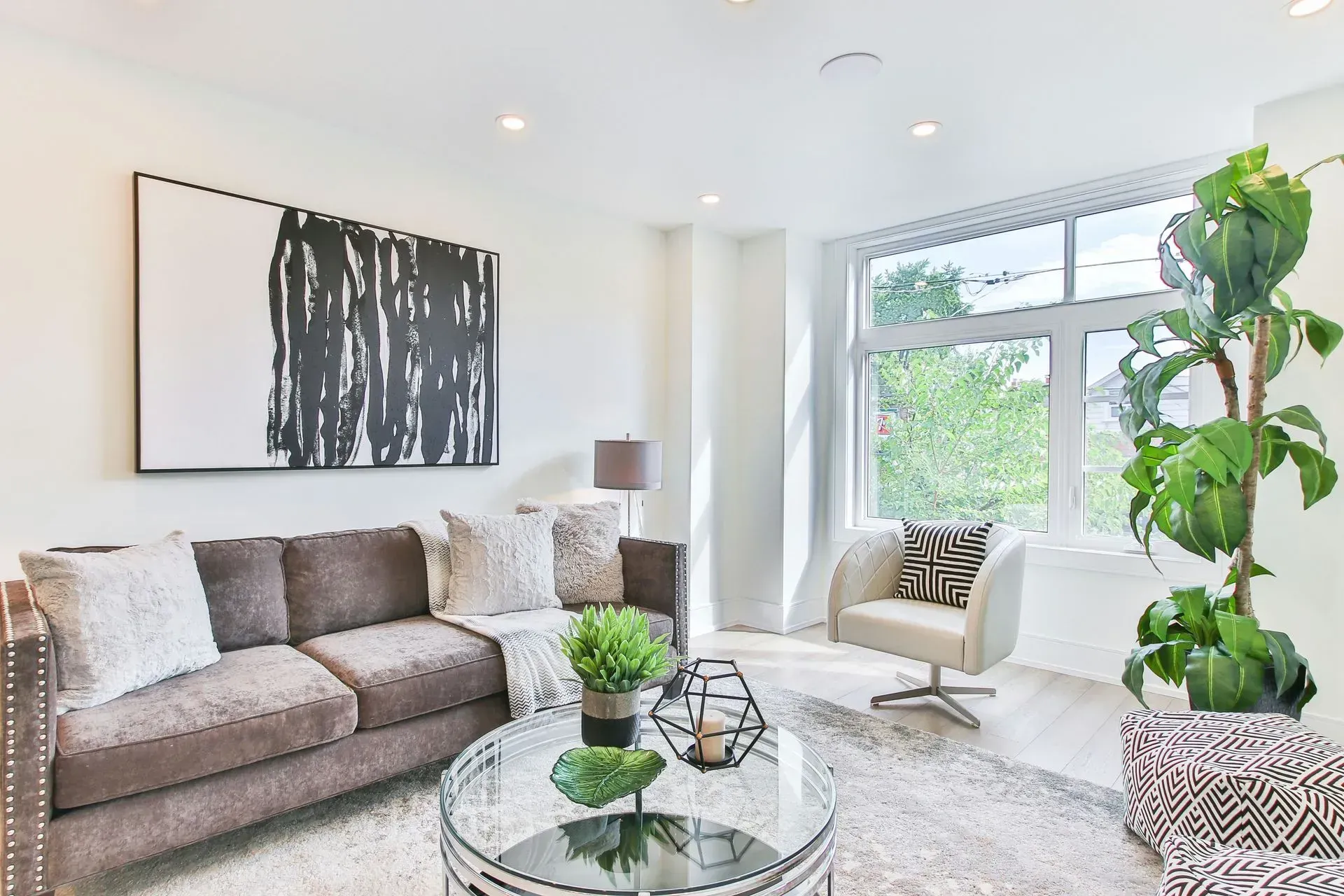 Bright modern living room with gray sofa, abstract wall art, large window, and potted plants