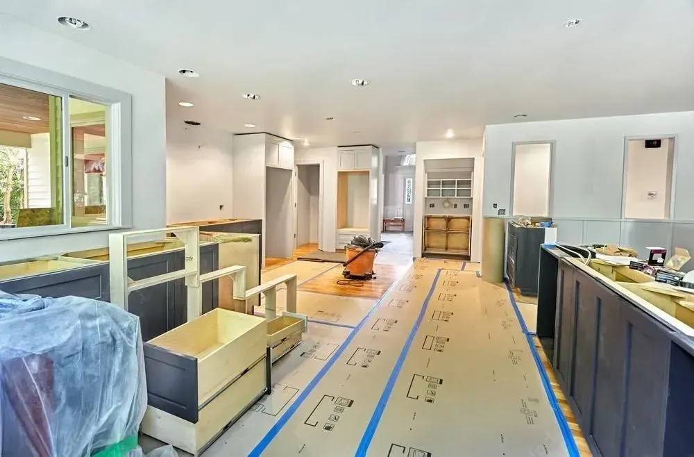 Kitchen renovation in progress with cabinets, appliances, and protective floor covering in a bright room