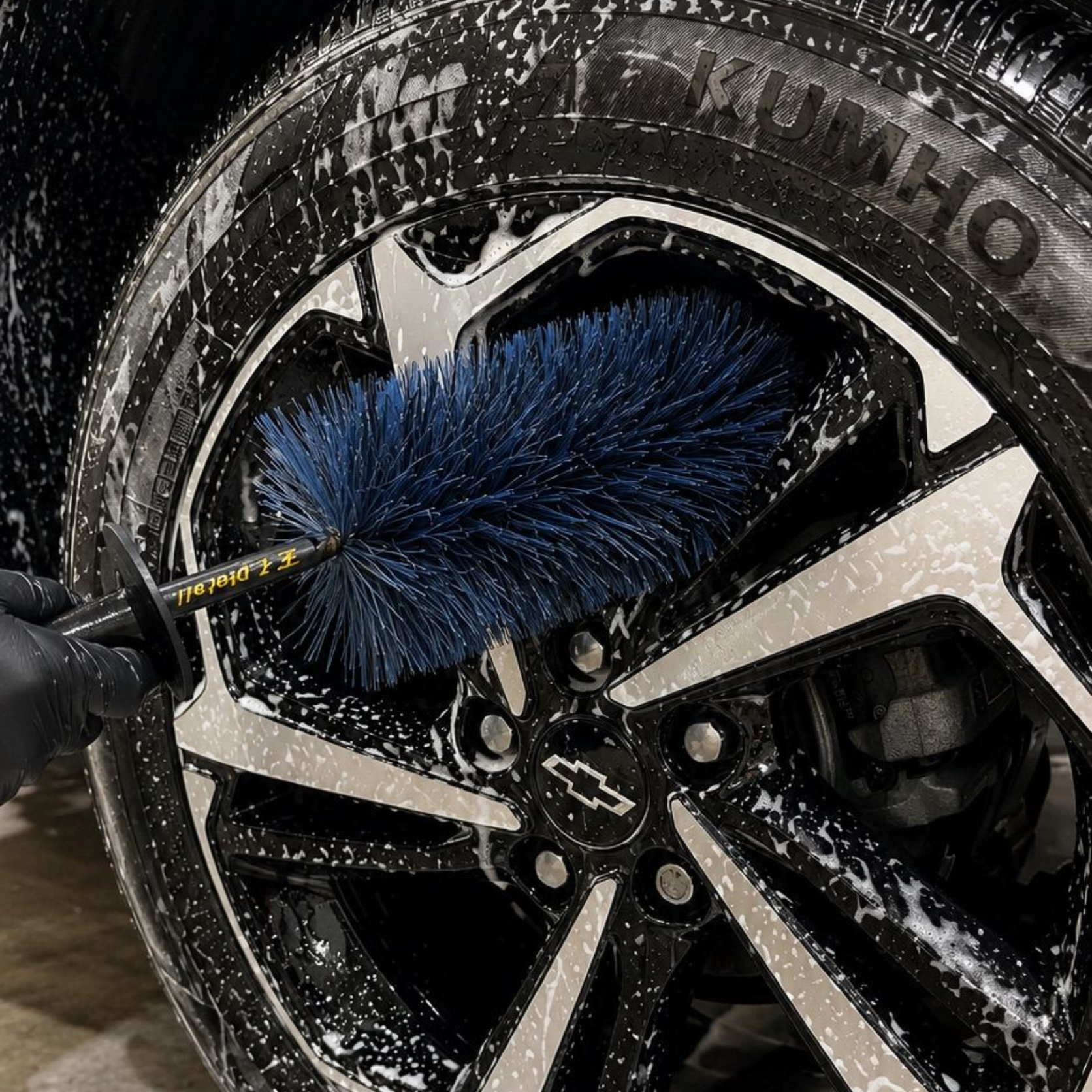 Blue wheel brush cleaning a black car rim covered in soap suds