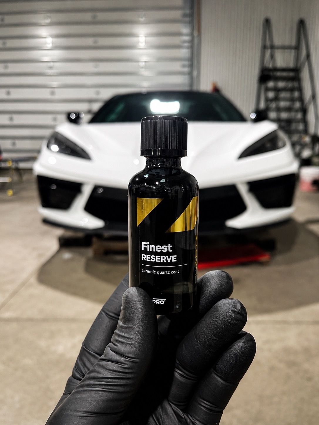 Gloved hand holding a bottle of tire shine in front of a white sports car in a garage