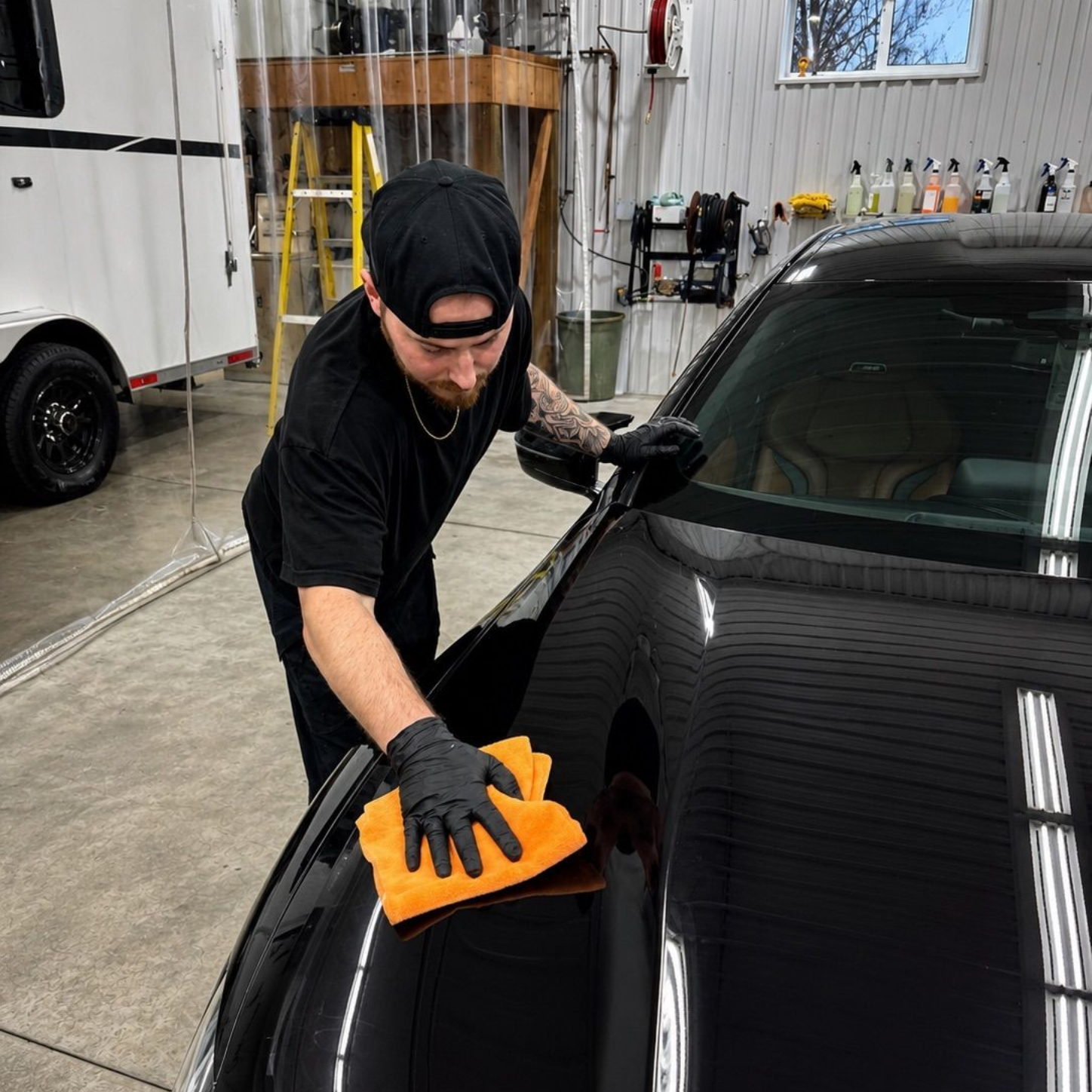 Worker wiping a black car hood with an orange cloth in a garage workshop