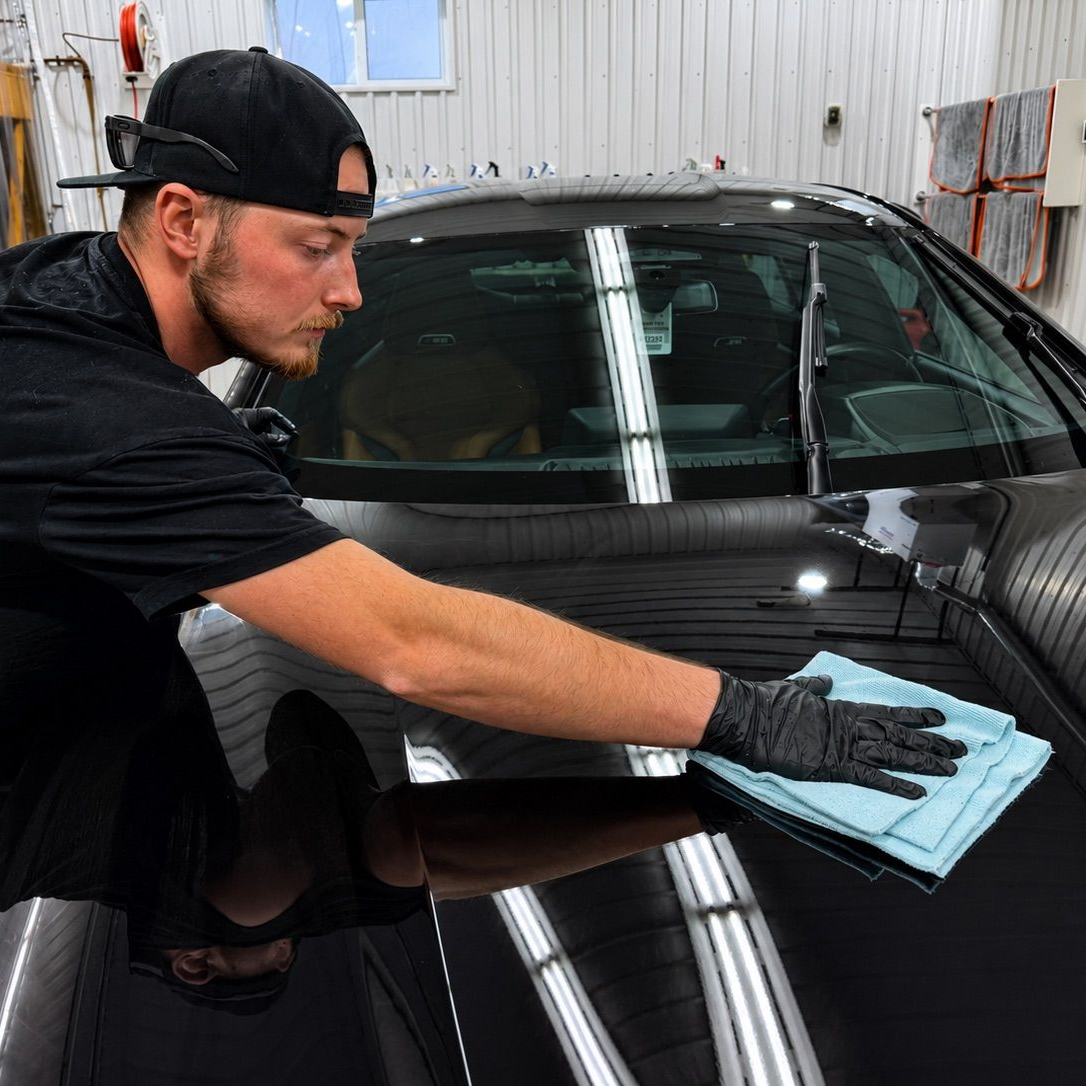 Detailing worker wiping a black car with a blue cloth in a garage