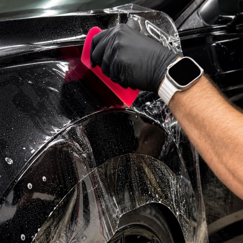 Gloved hand wiping water off a black car with a pink cloth