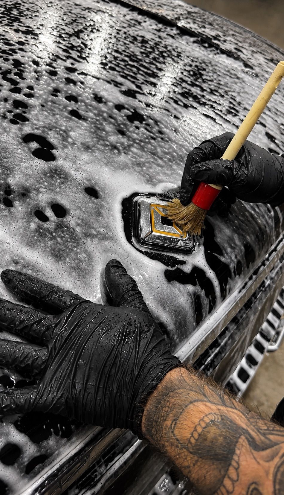 Gloved hands scrubbing a snow-covered car windshield with a brush and sponge