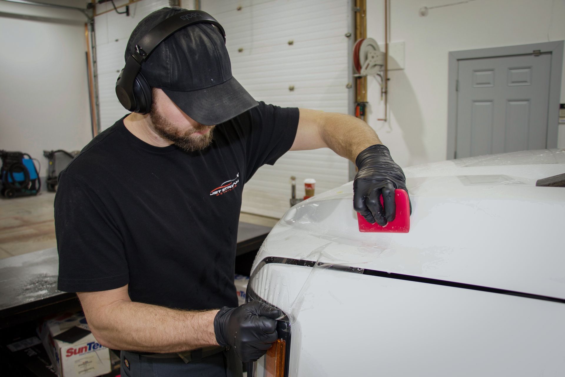 A man wearing headphones and a hat is working on a car.